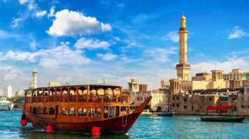 A dhow, traditional ship, sails past the Grand Bur Masjid in Dubai, UAE.