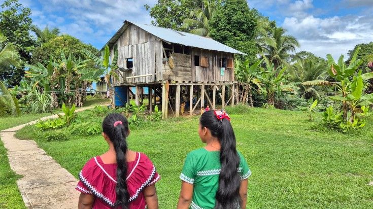 Two indigenous women of Isla Popa, a traditional house and lush green space