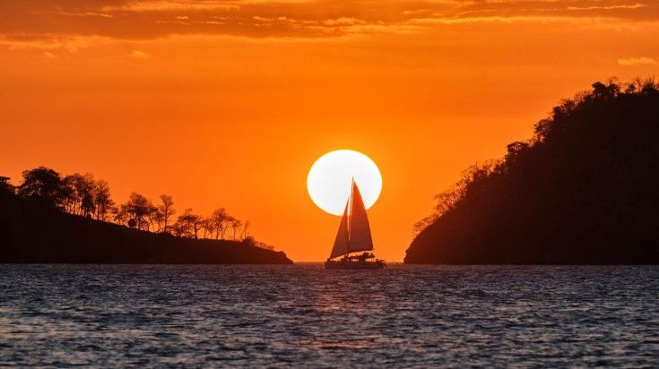 A sailboat on the Pacific with full sails up is silhouetted in front of the setting sun. A sailboat on the Pacific with full sails up is silhoutted in front of the