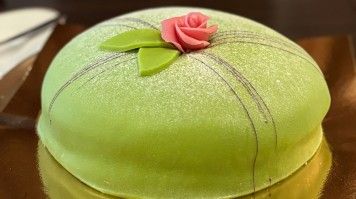Princess cake with green marzipan, powdered sugar, & a pink rose.