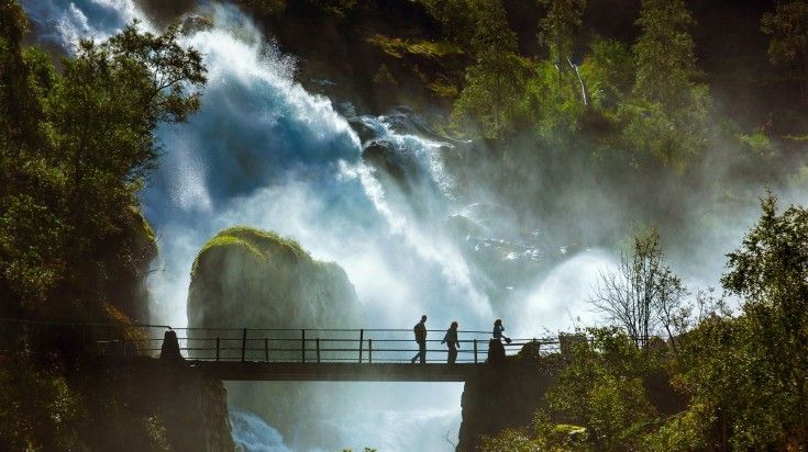 People walking on the bridge near Briksdal Glacier' waterfall in Norway.