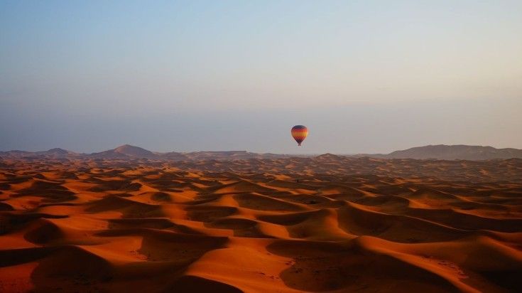 A hot air balloon flies over a desert landscape in Dubai.