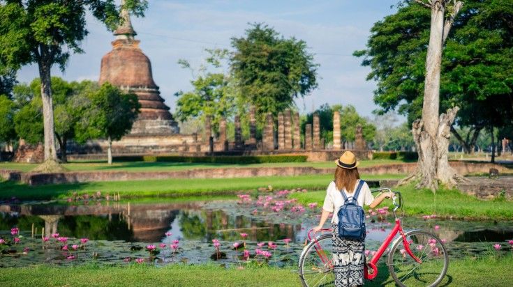 A young woman with her bicycle in Sukhothai Historical Park on a clear day.