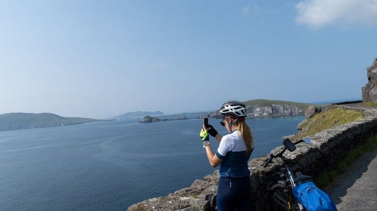 A woman traveling by bicycle taking pictures at Dingle Peninsula on a clear
