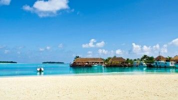 Sandy beaches and blue waters of Kandooma island with stilt houses & boats