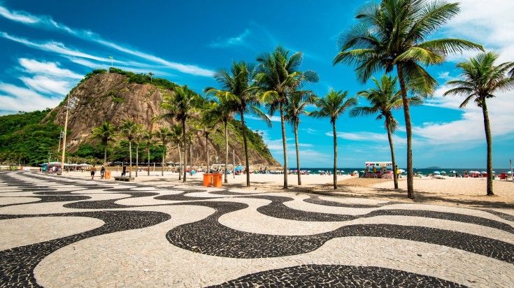 Mosaic sidewalk in Copacabana beach, palm trees and the Leme mountain.