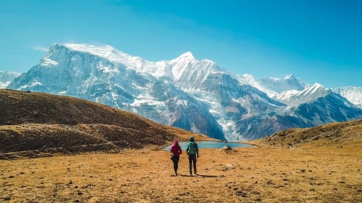 Two hikers walking towards a breathtaking panorama of snow-capped mountains