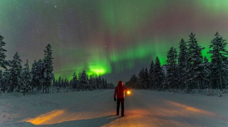 A man in the red jacket admiring the beauty of Northern Lights in Lapland.