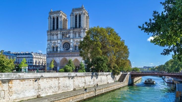 The view of Notre Dame Cathedral on the side of the river on a sunny day.