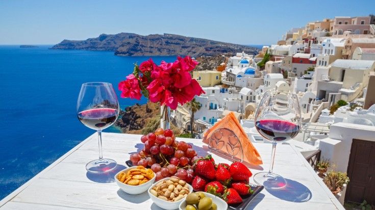 Wine, snacks and fruits on the table with a view of Santorini on a clear da
