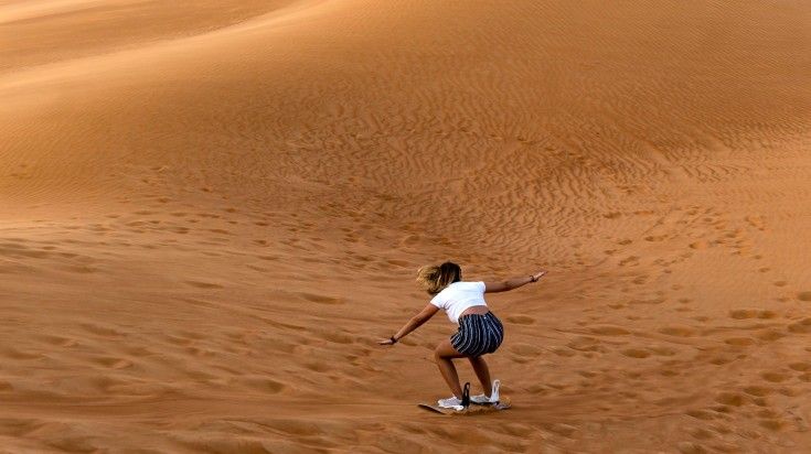 Young girl sandboarding in the Dubai desert.