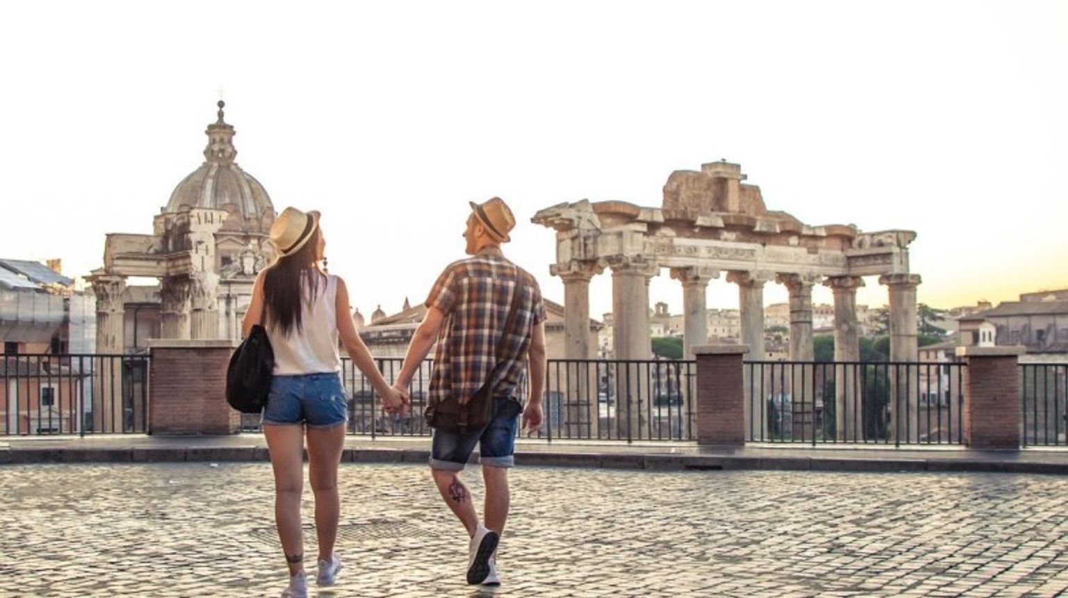 Step back in time and visit the Roman Forum, one of the must-see historical sites and top places to visit in Italy, brimming with ancient ruins and stories. A happy couple walking hand in hand towards Roman Forum, one of the best places to visit in Italy.