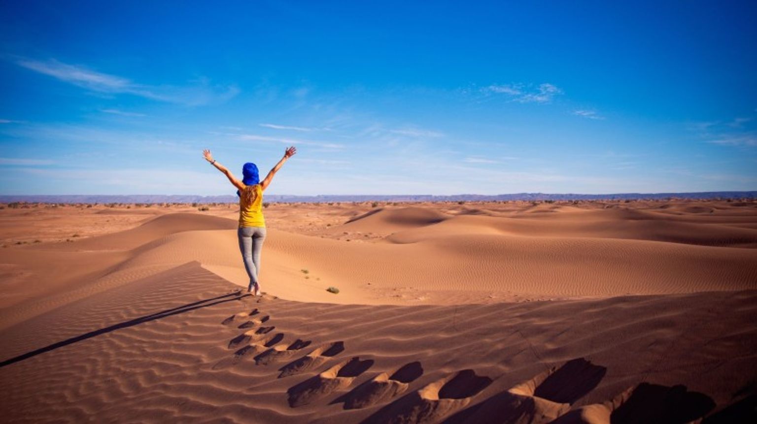A woman tourist with open arms in the sand dune in the Sahara Desert on her 10 days in Morocco.