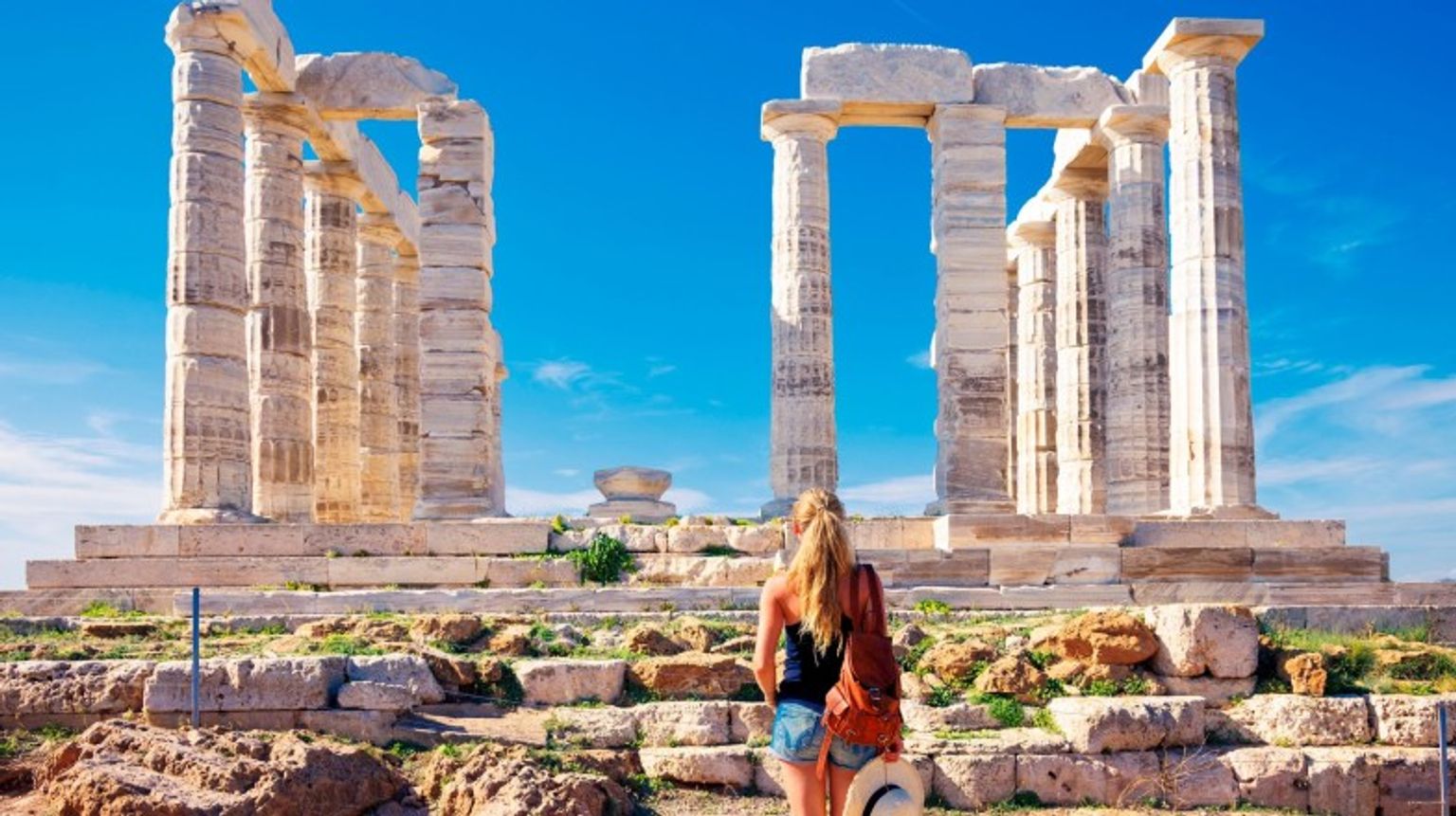 Rear view of female tourist admiring the beauty of old Greek temple ruins during her 5 days in Greece.