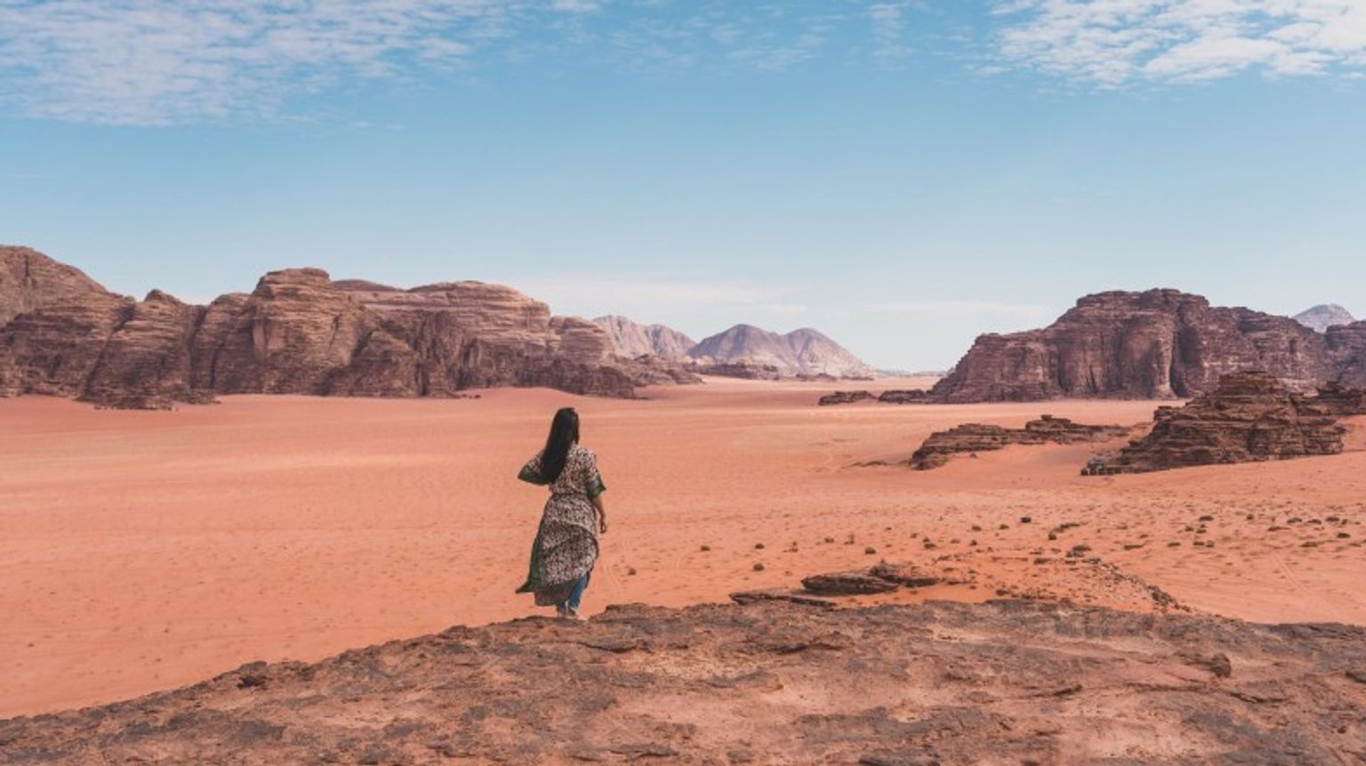 A woman standing on a top of mountain and enjoying the landscape of Wadi Rum desert during her 5 days in Jordan.