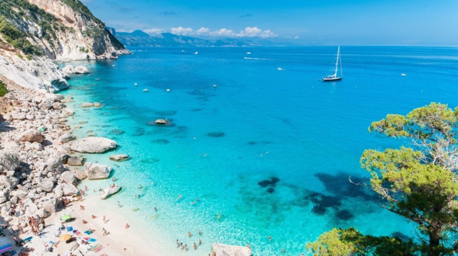 Visit Cala Goloritze, one of the best beaches in Italy, and discover its stunning turquoise waters, dramatic cliffs, and serene beauty. Aerial view of Cala Goloritze, one of the best beaches in Italy, on a clear day.