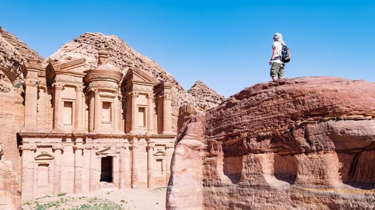 A man on top of the rock is admiring the beauty of Petra on a sunny day in Jordan in August.