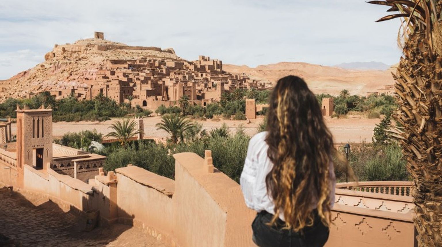 A woman sitting in the fence admiring the beauty of Ait-Ben Haddou.