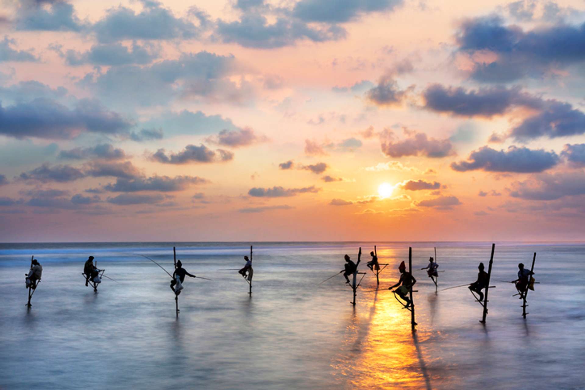 A group of fishermen stand on stilts in a sea in Sri Lanka at sunset