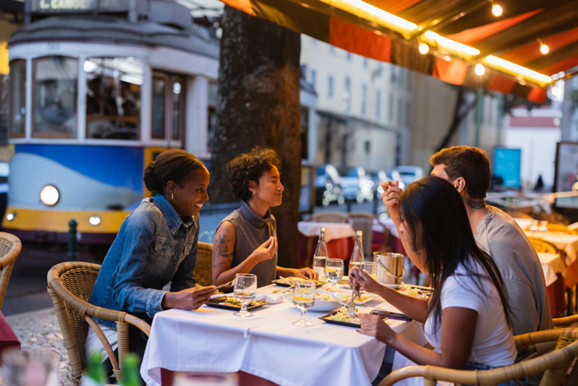 A group of friends enjoy meal around a table in Lisbon as the tram goes by