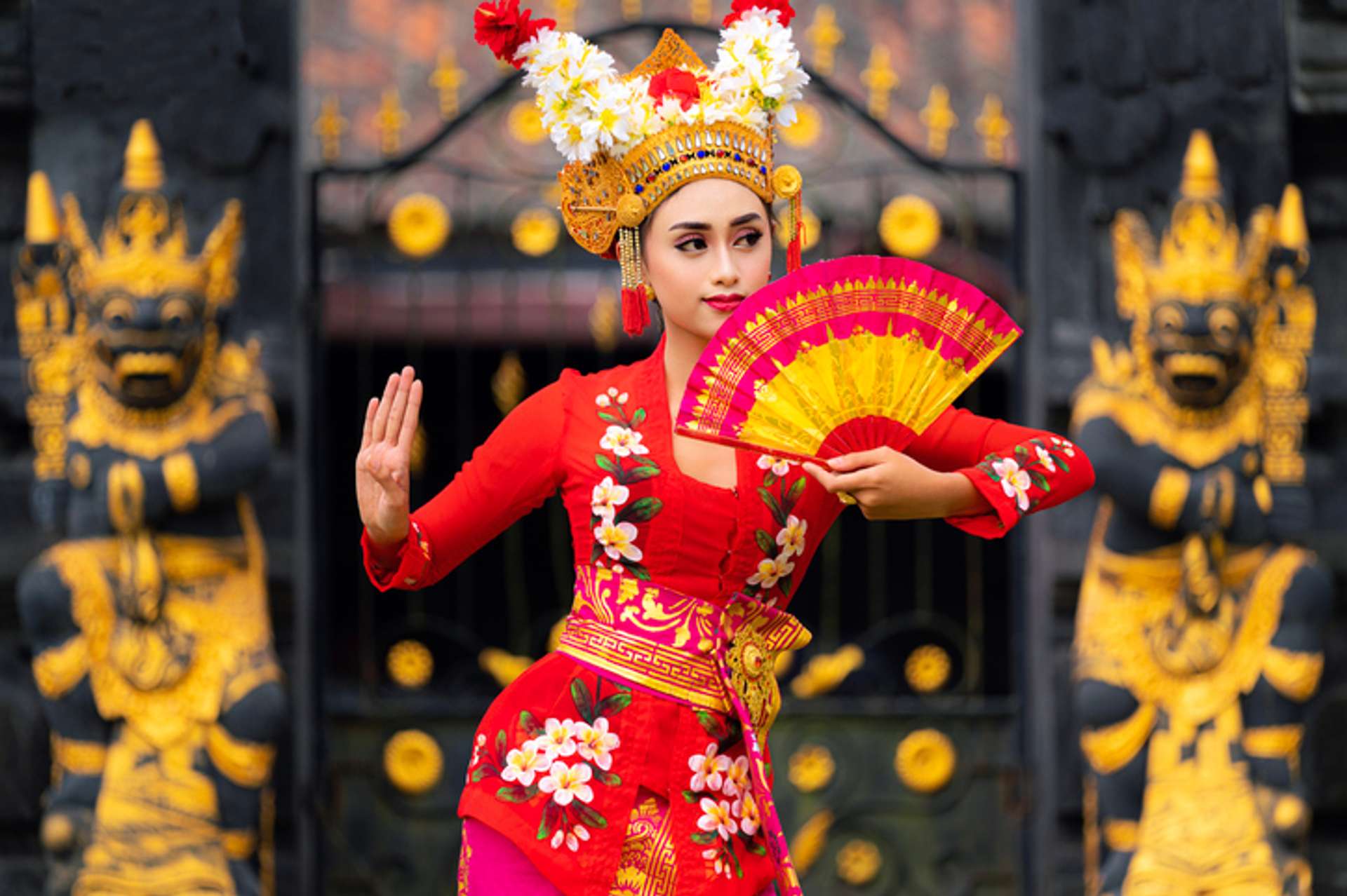 A woman in traditional Indonesian dance costume and fan in hand poses