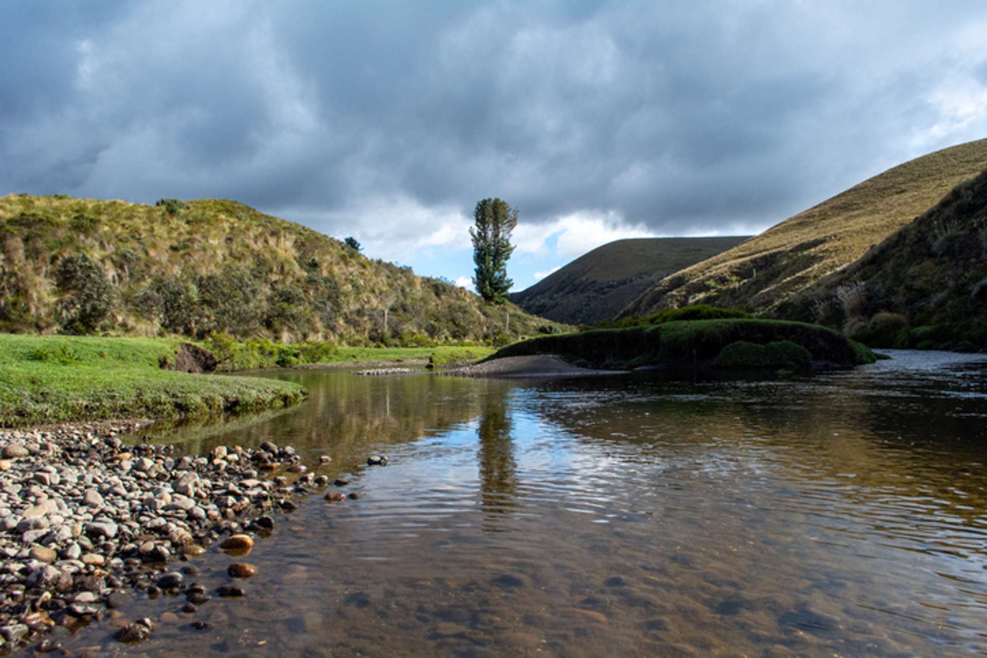View of a lake surrounded by small hills and clouded sky in Llanganatas National Park in Ecuador