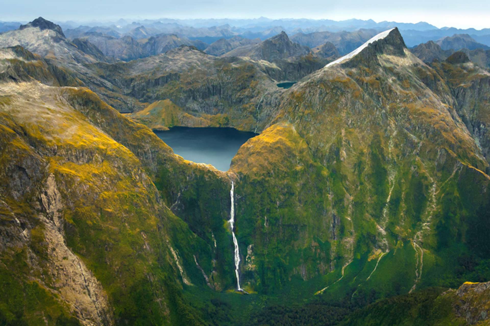 Aerial view of a lake surrounded by hills, with a waterfall falling down