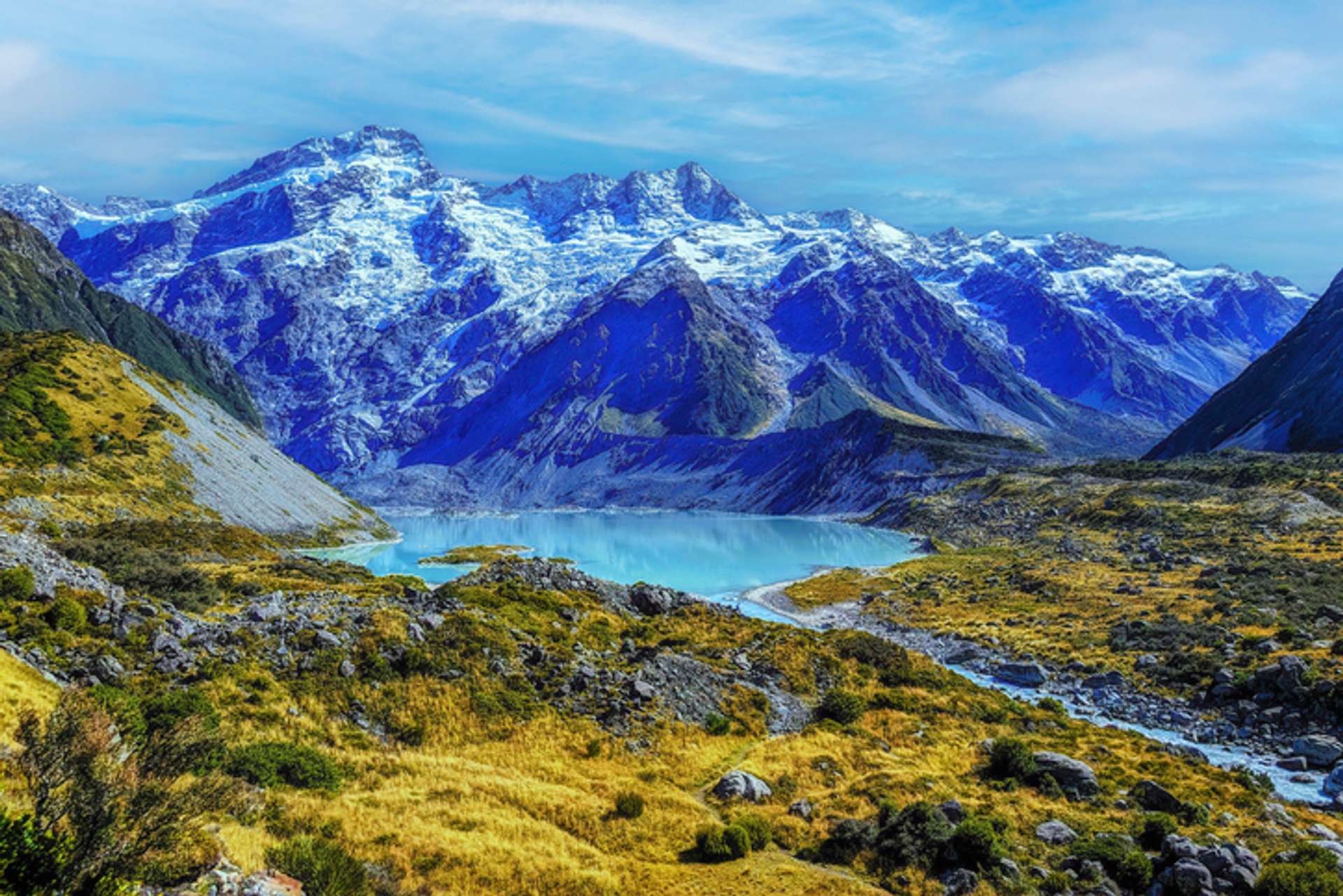 A turquoise lake with snow-capped mountains on one side and rocky grasslands on three sides