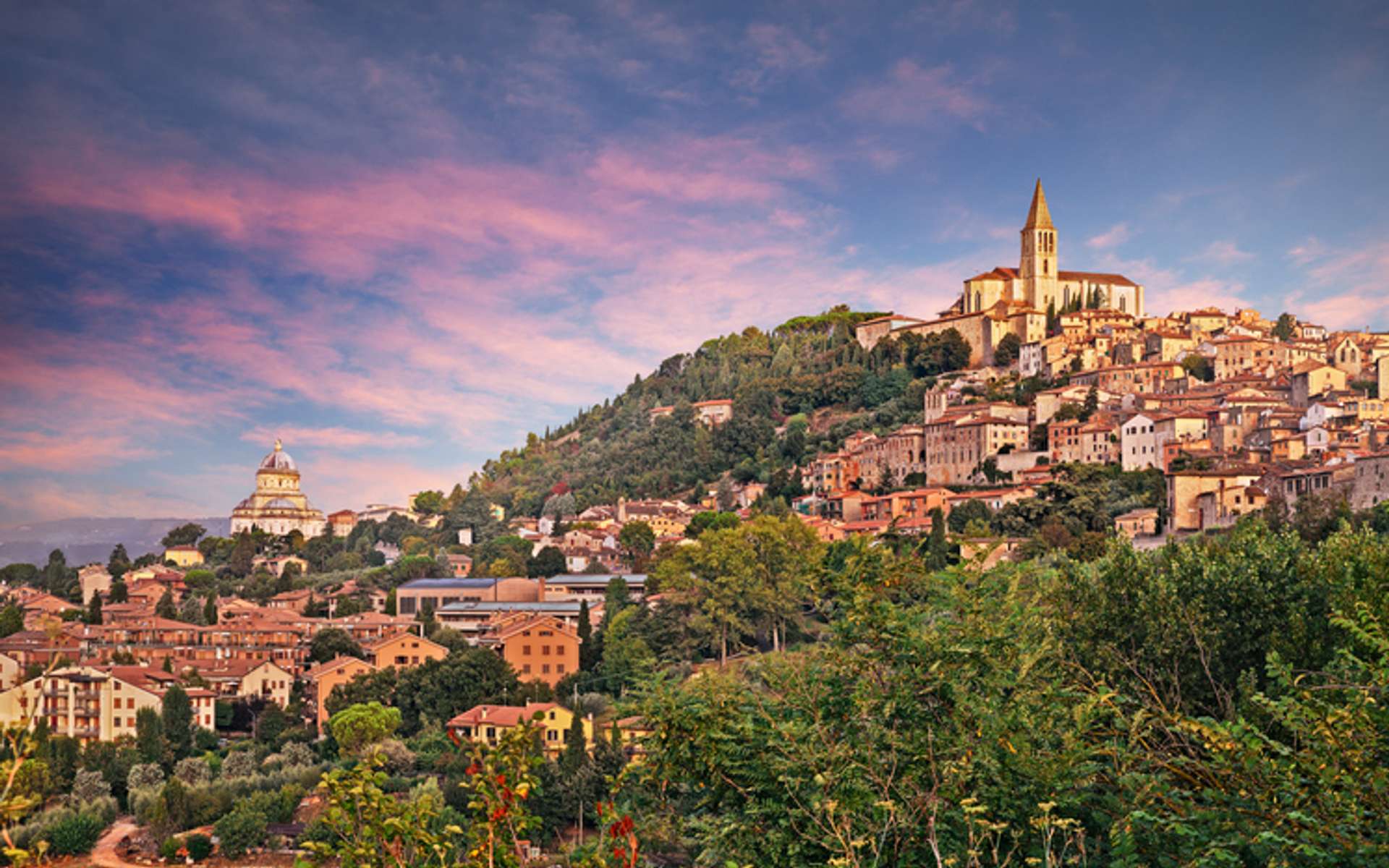 View of a green hill with houses and buildings rising from it with blue sky with pink clouds