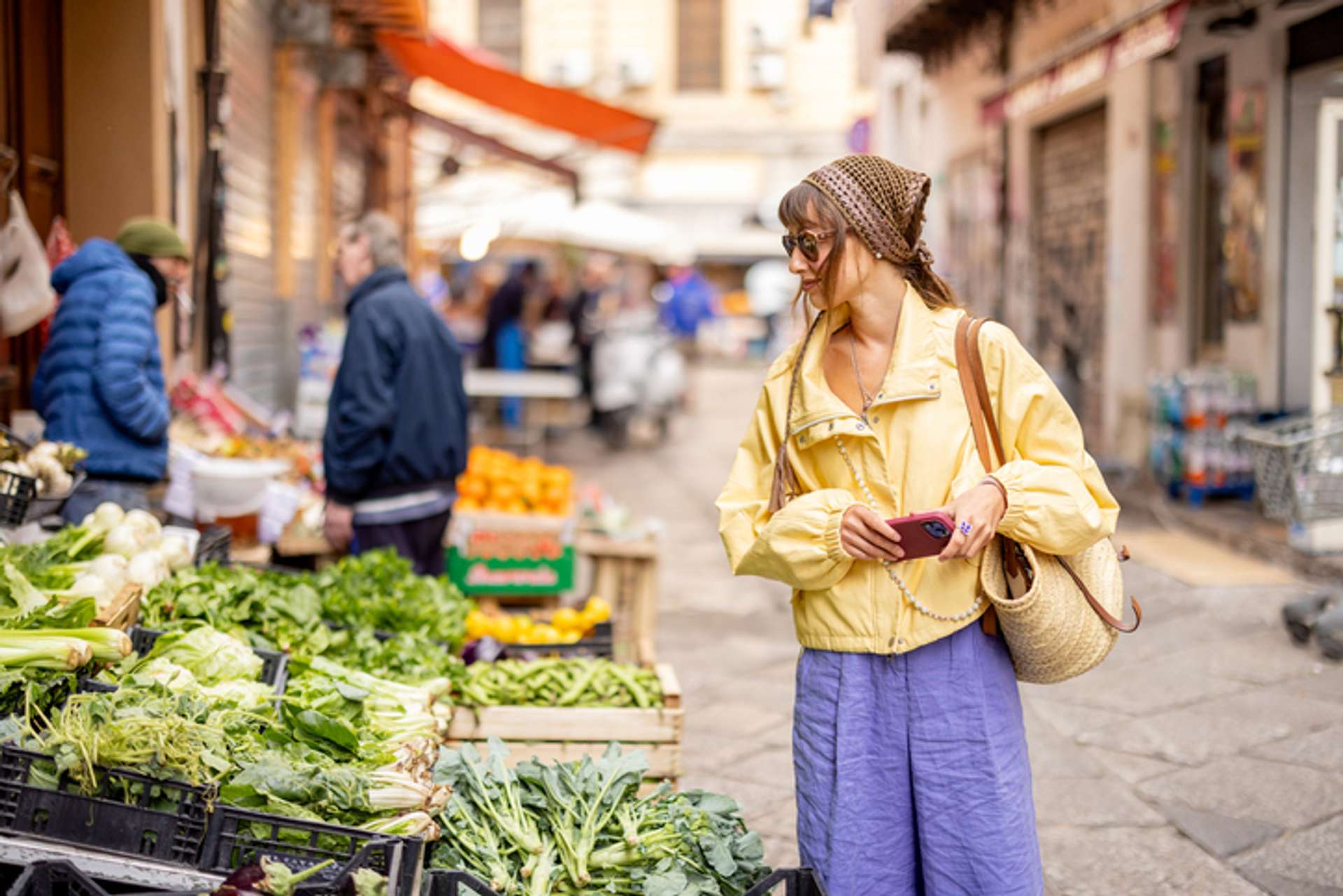 A woman on the streets looks at green vegetable at the market