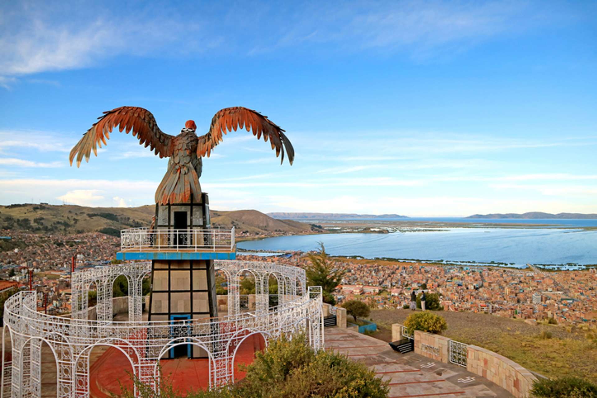 Aerial view of a condor statue overlooking a populated town settled on the shores of a lake