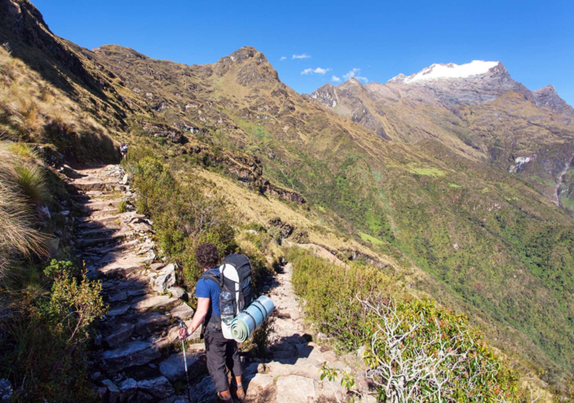 A trekker on a stepped trail with view of mountains and hills that slope down into a valley