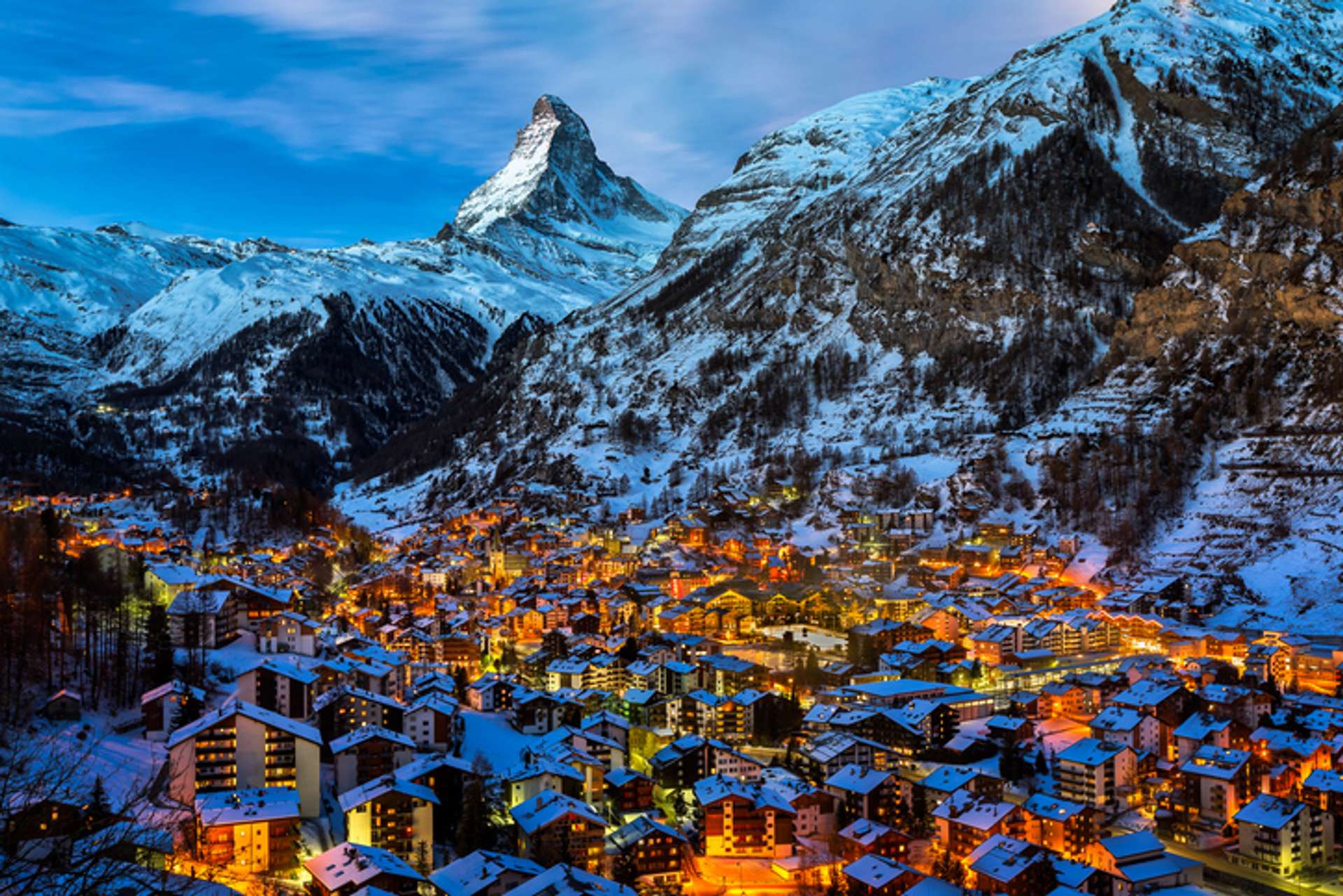 snowy mountain with town beneath glowing in evening lights