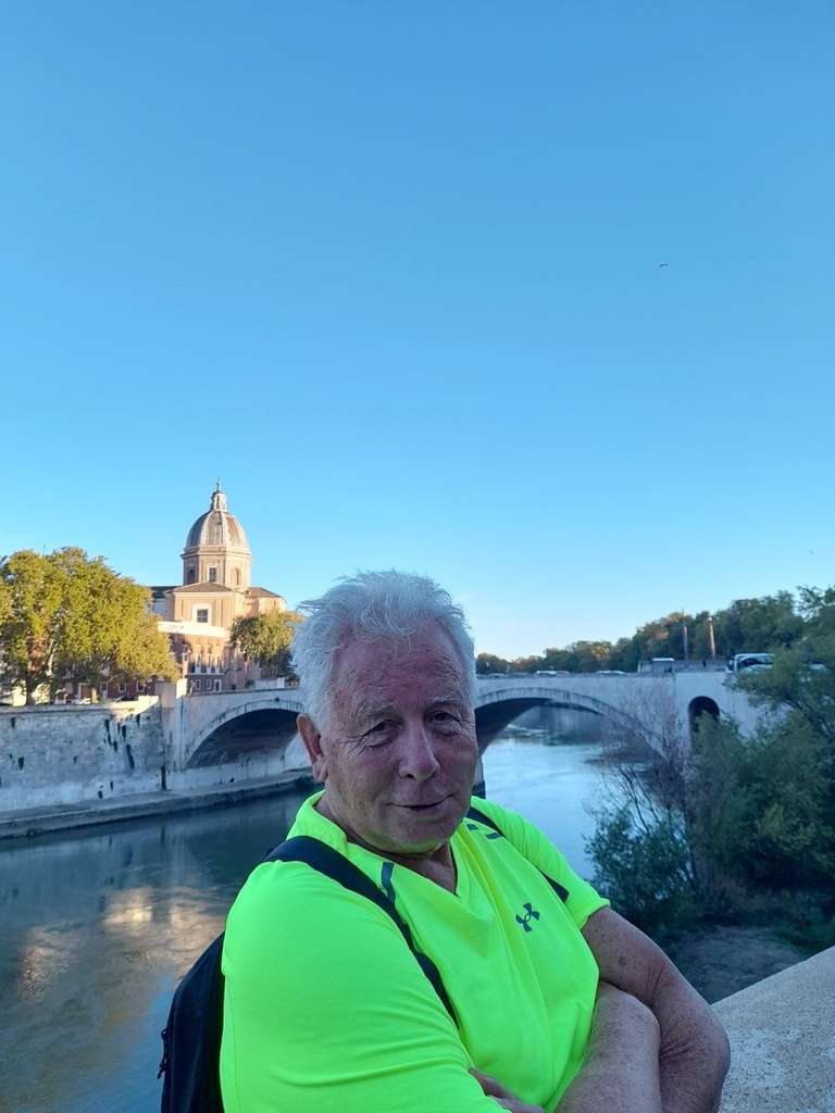 An elderly traveler in green tshirt next to a canal with an ancient structure in the background