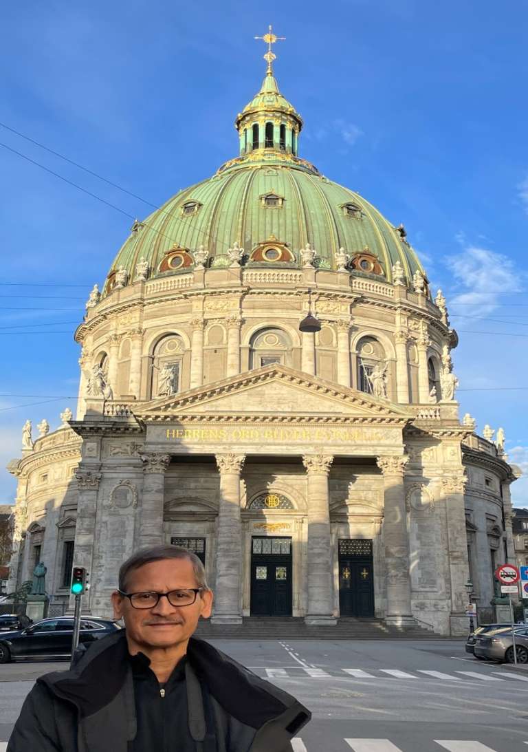 An elderly man poses in front of an ancient European structure