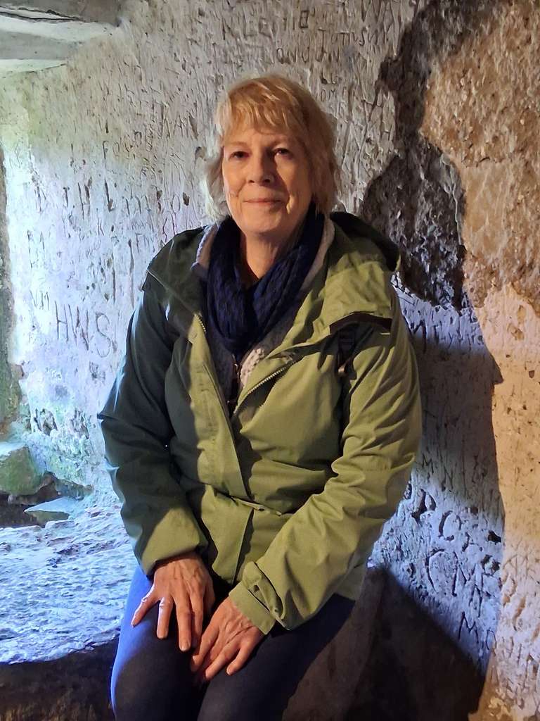An older lady in green jacket poses inside an old building