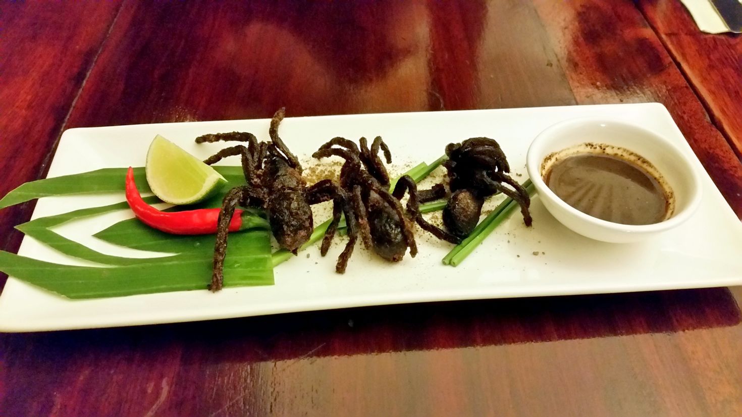 Fried tarantula on a plate garnished with leaves, lemons, chili and sauce. 