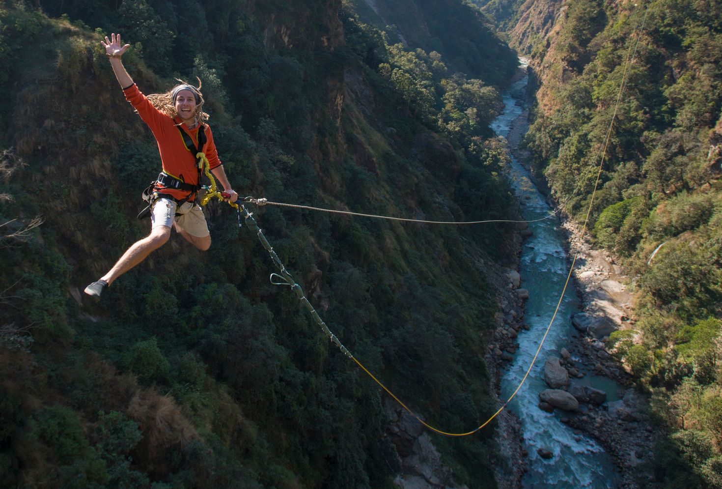 A woman swings from a cliffs with the Bhotekoshi river underneath. 