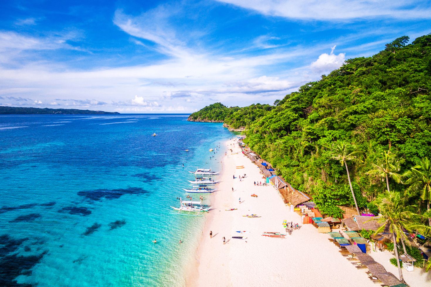 The shoreline of Boracay with water on one side and forest in the other on a clear day. 