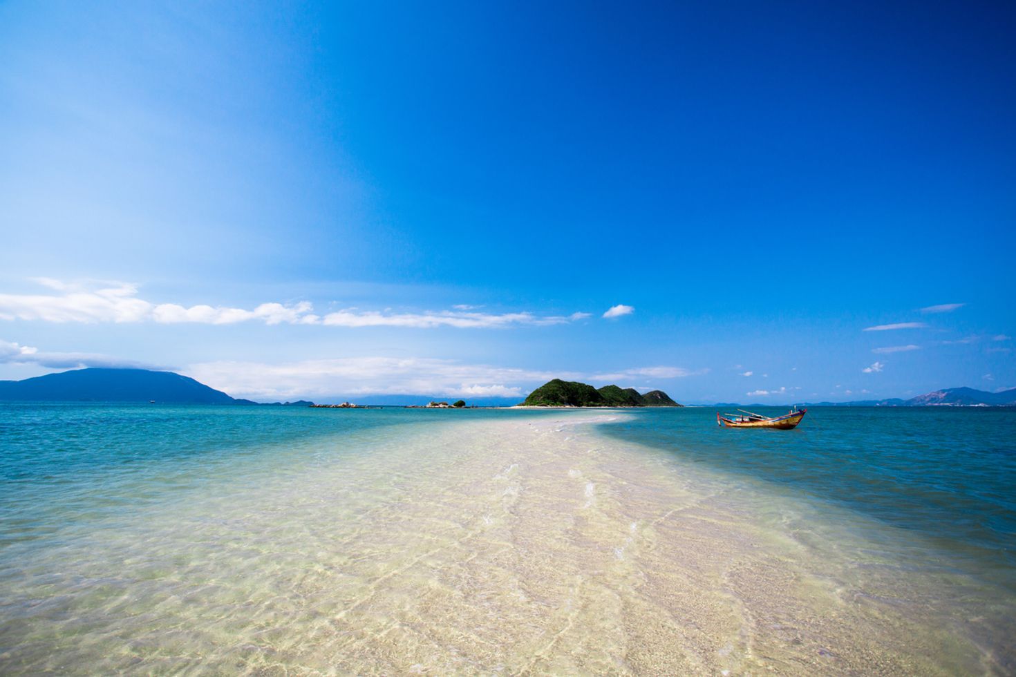 Sand covered with water on both sides with hills in the distance at Nha Trang beach. 