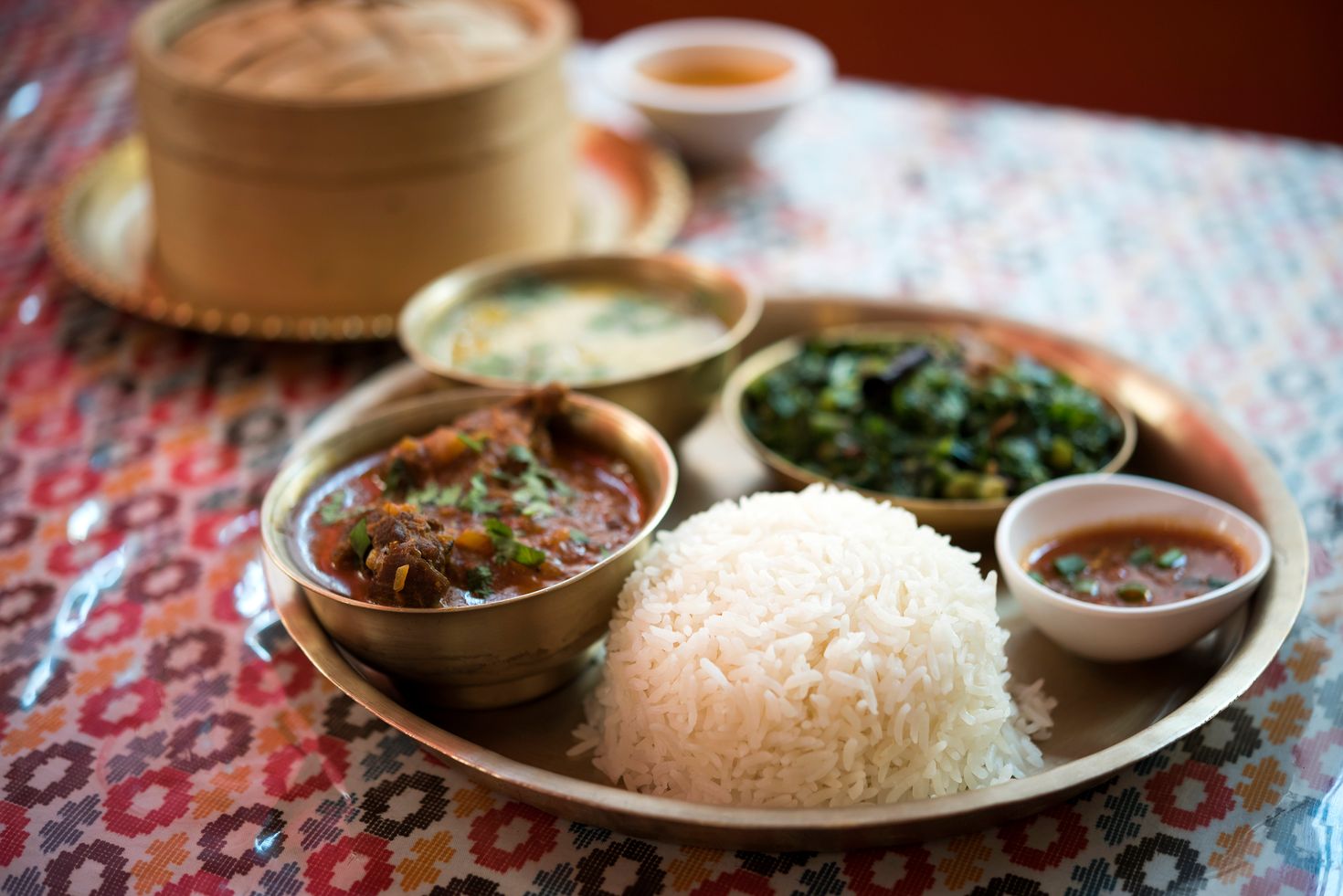 Nepalese food - Dal Bhat served neatly on a plate with rice, lentil soup, fresh vegetables and meat curry set on a table. 