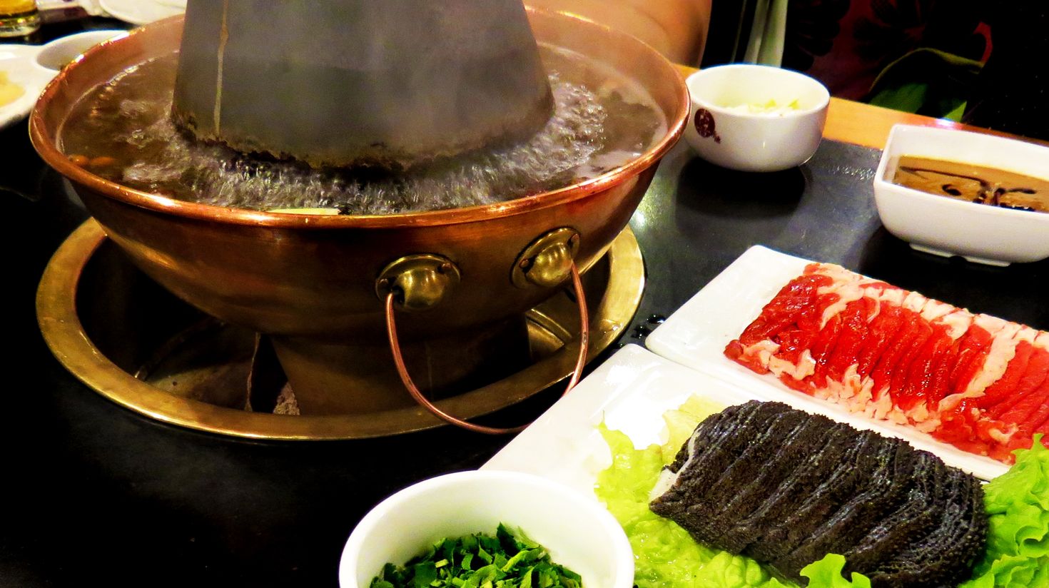 Water boiling in hot pot, vegetables, sauce and slices of meat