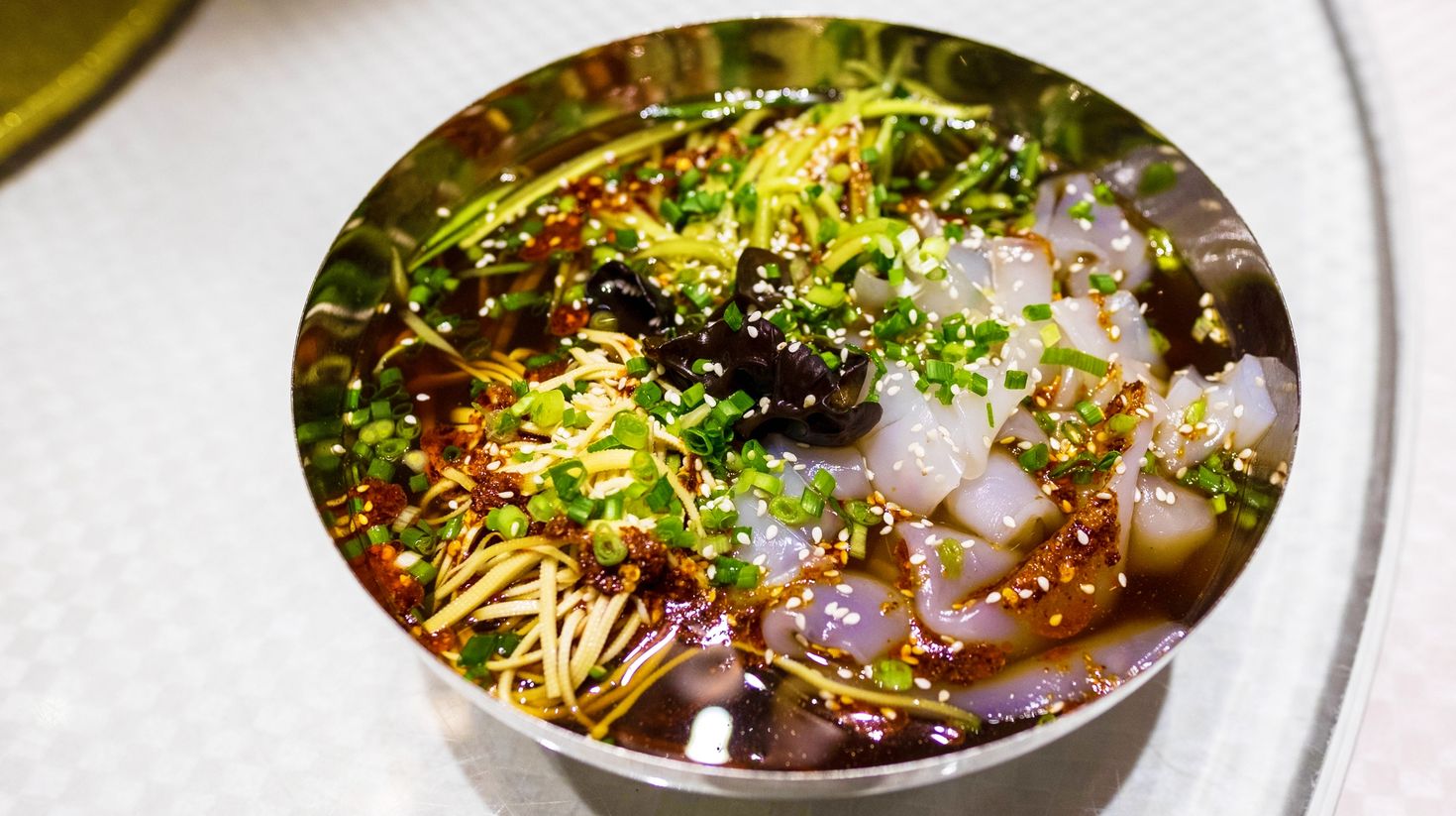 A bowl containing soupy flour noodles, onion leaves and sesame seeds