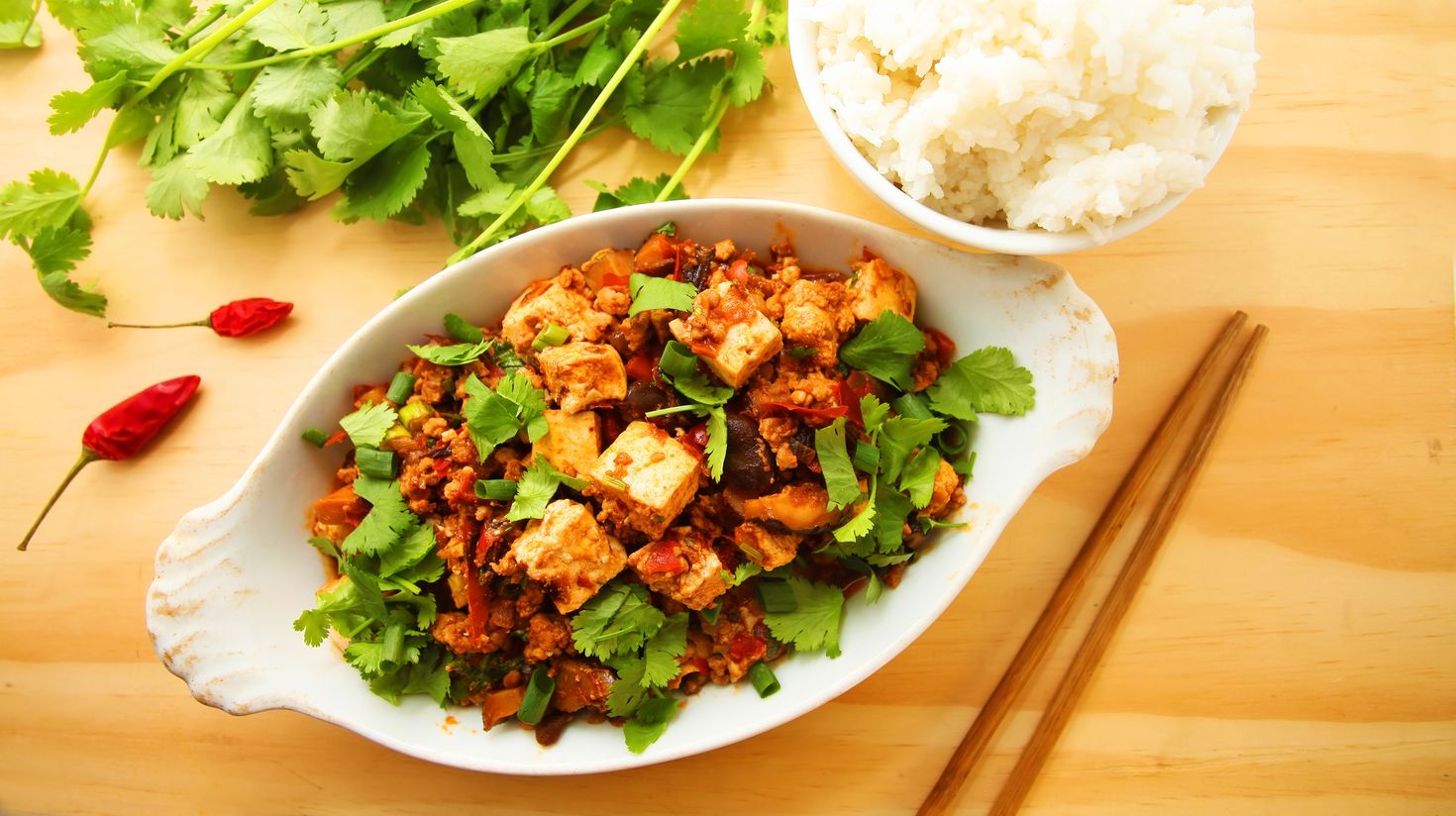 Coriander and chopsticks with a bowl of rice and a bowl of tofu