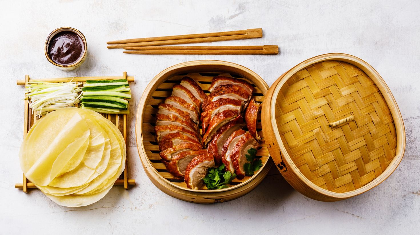 Slices of meat in a wooden container, rolled dough, sauce and chopsticks