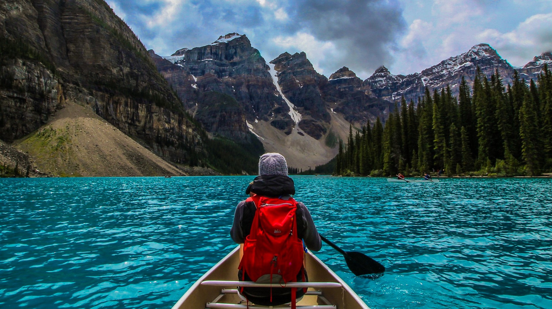 A traveler paddling on a boat on blue water during the day with mountains all around.