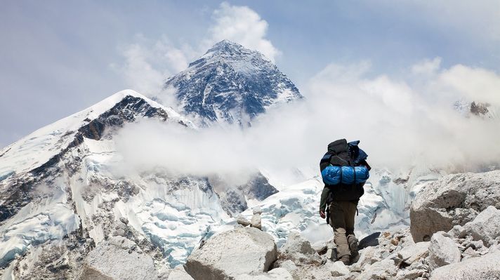 A trekker walking to Everest Base Camp with the tip of the Mount Everest in the distance. 