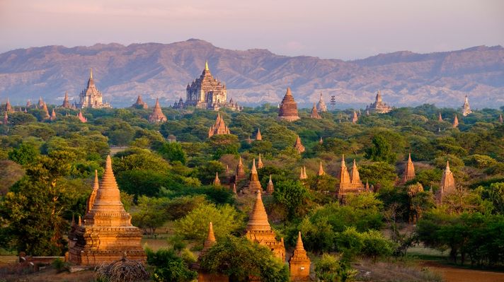 Bagan's Holy sites and historical monuments with hills in the distance during sunset in Myanmar. 