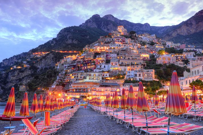 The Amalfi Coast with rows of sunbeds, colorful umbrellas and illuminated houses in Italy. 