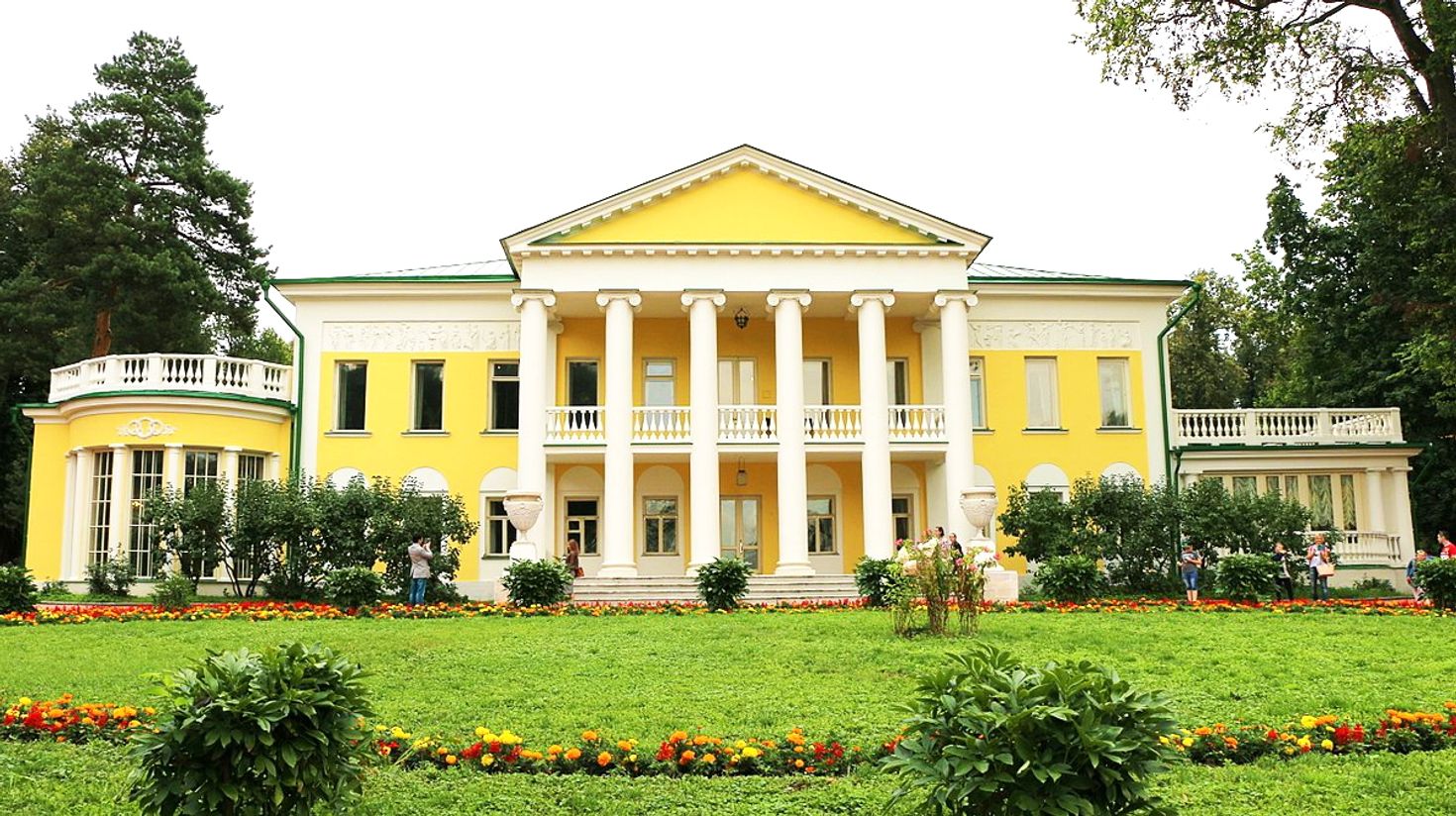 View of a yellow coloured mansion with a garden in front